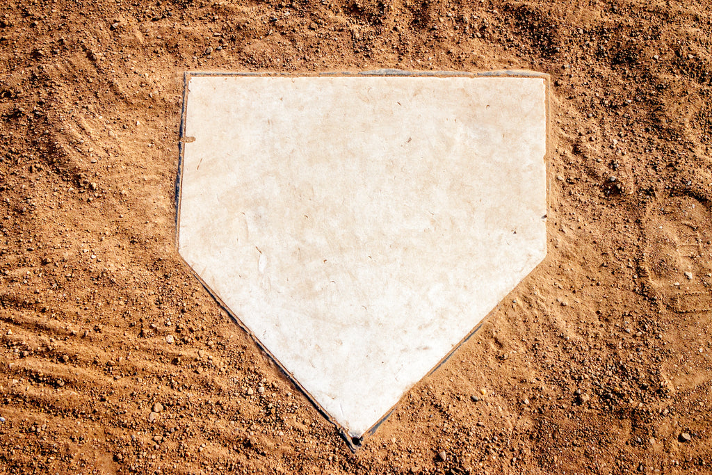 Overhead view of a clean white home plate on a sandy baseball infield. Symbolic start of every at-bat, perfect for baseball gear branding or team imagery.